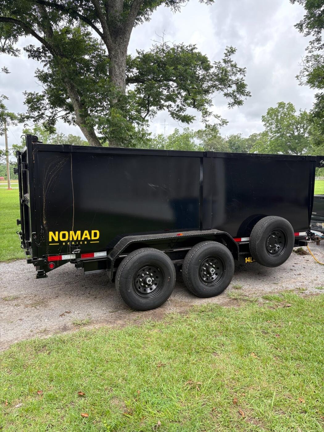 Black Nomad brand tandem axle dump trailer with yellow lettering parked on grass