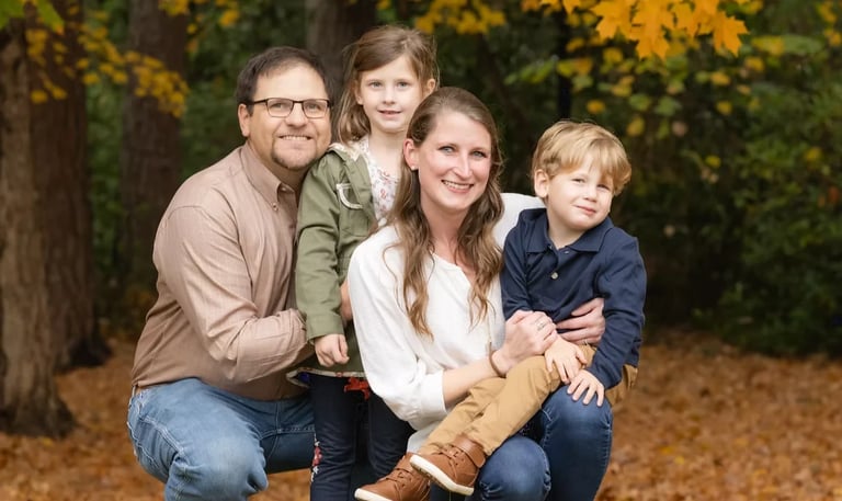 Family of four posing together outdoors in autumn, surrounded by yellow foliage and trees
