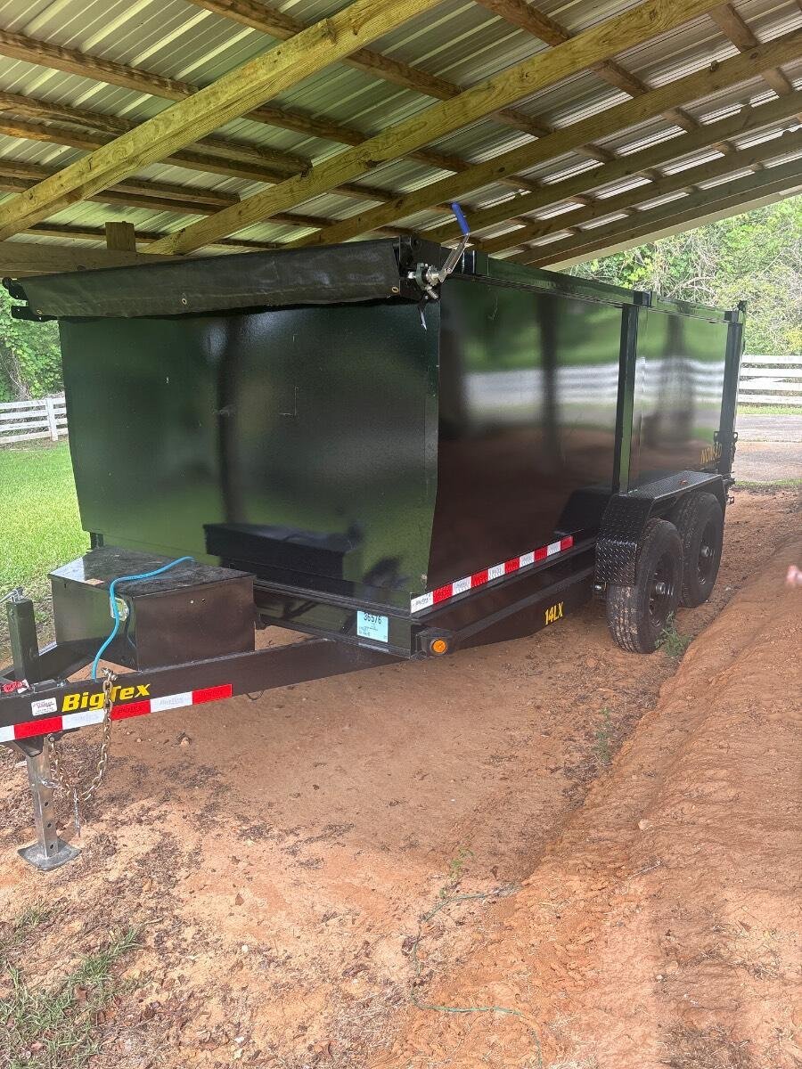 Black enclosed horse trailer with red and white striped bumper parked under a covered structure on a dirt driveway